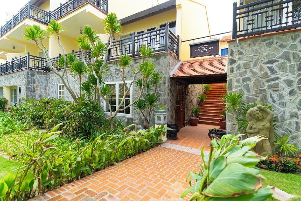 A spa building with a stone facade, a wooden staircase, and a well-maintained garden with tropical plants.