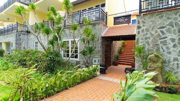 A spa building with a stone facade, a wooden staircase, and a well-maintained garden with tropical plants.