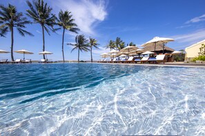 A clear pool with lounge chairs and umbrellas, surrounded by palm trees. - Victoria Hoi An Beach Resort & Spa (Da Nang)