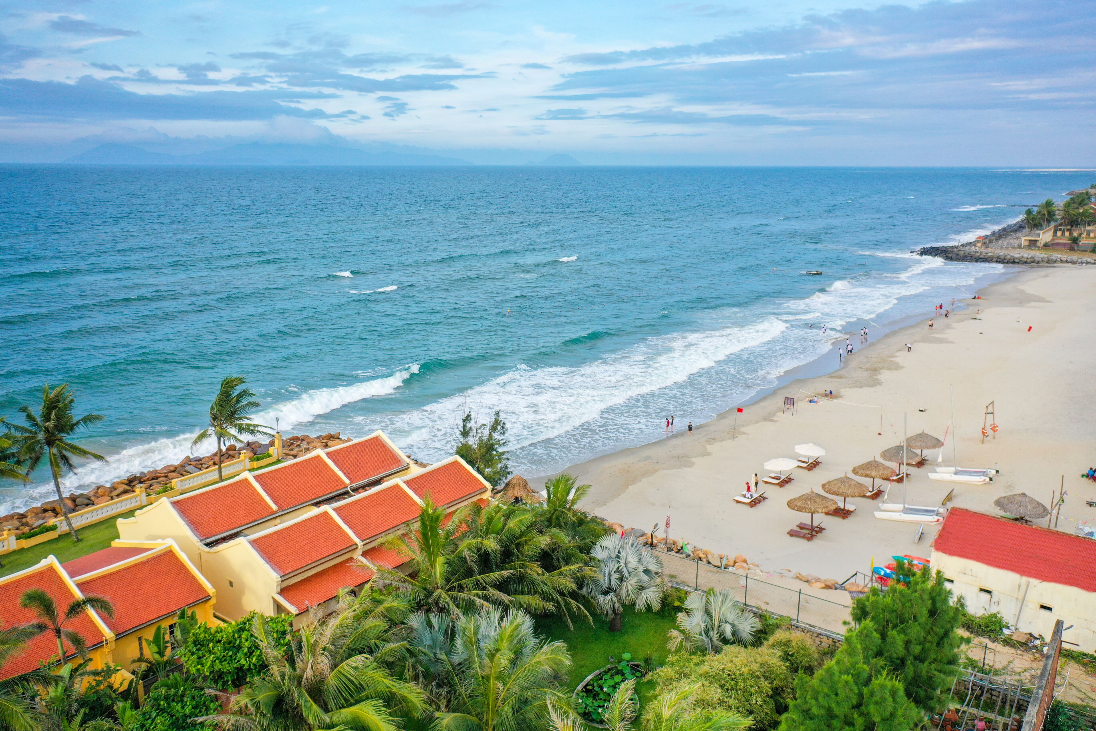 Una playa con una hilera de edificios amarillos con techos rojos, una playa arenosa y el océano.