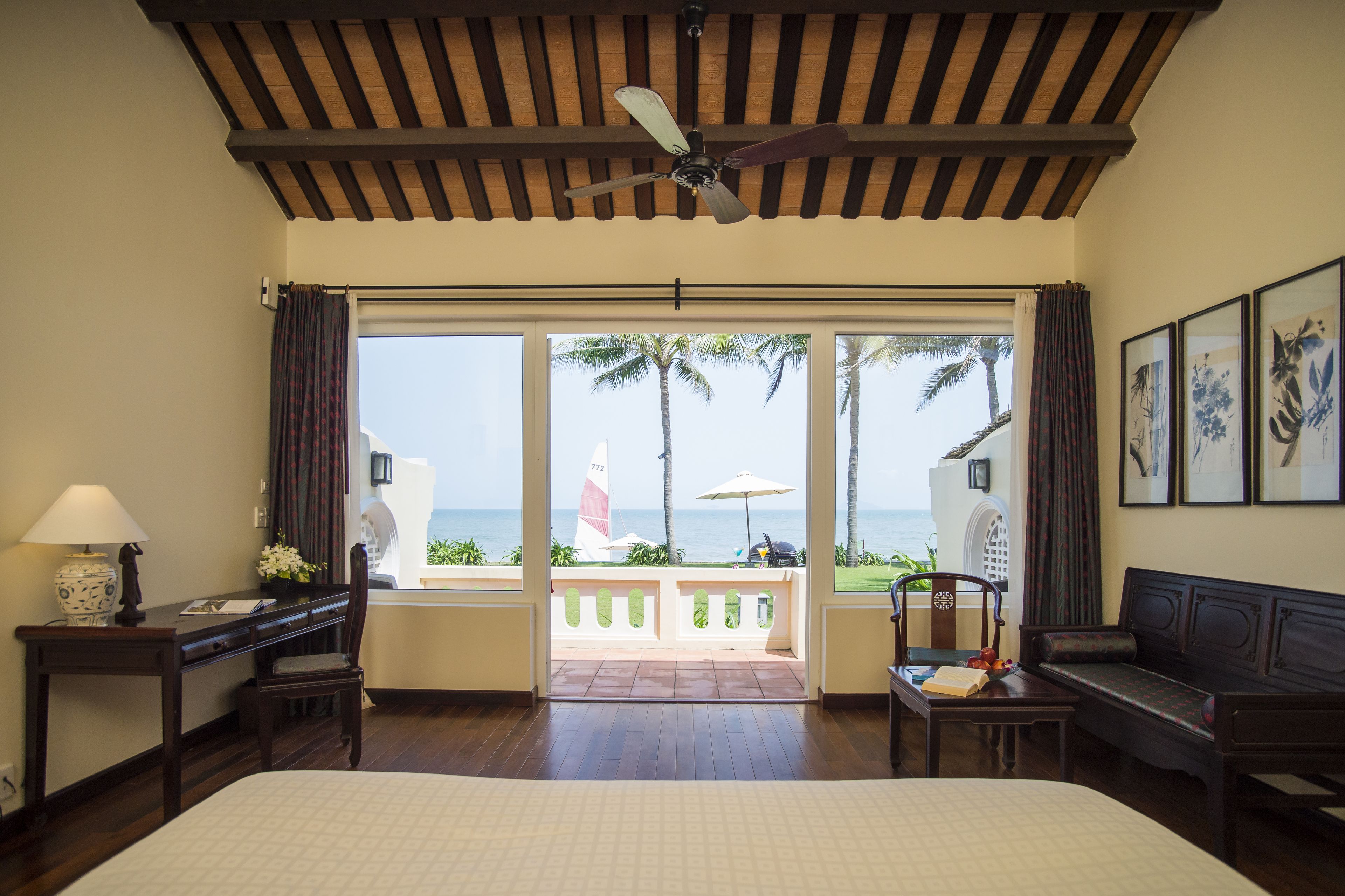 A hotel room with a bed, desk, chair, and a view of the ocean through large windows.