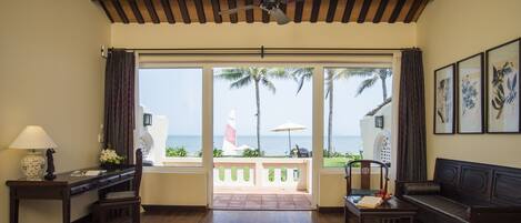 A hotel room with a bed, desk, chair, and a view of the ocean through large windows.