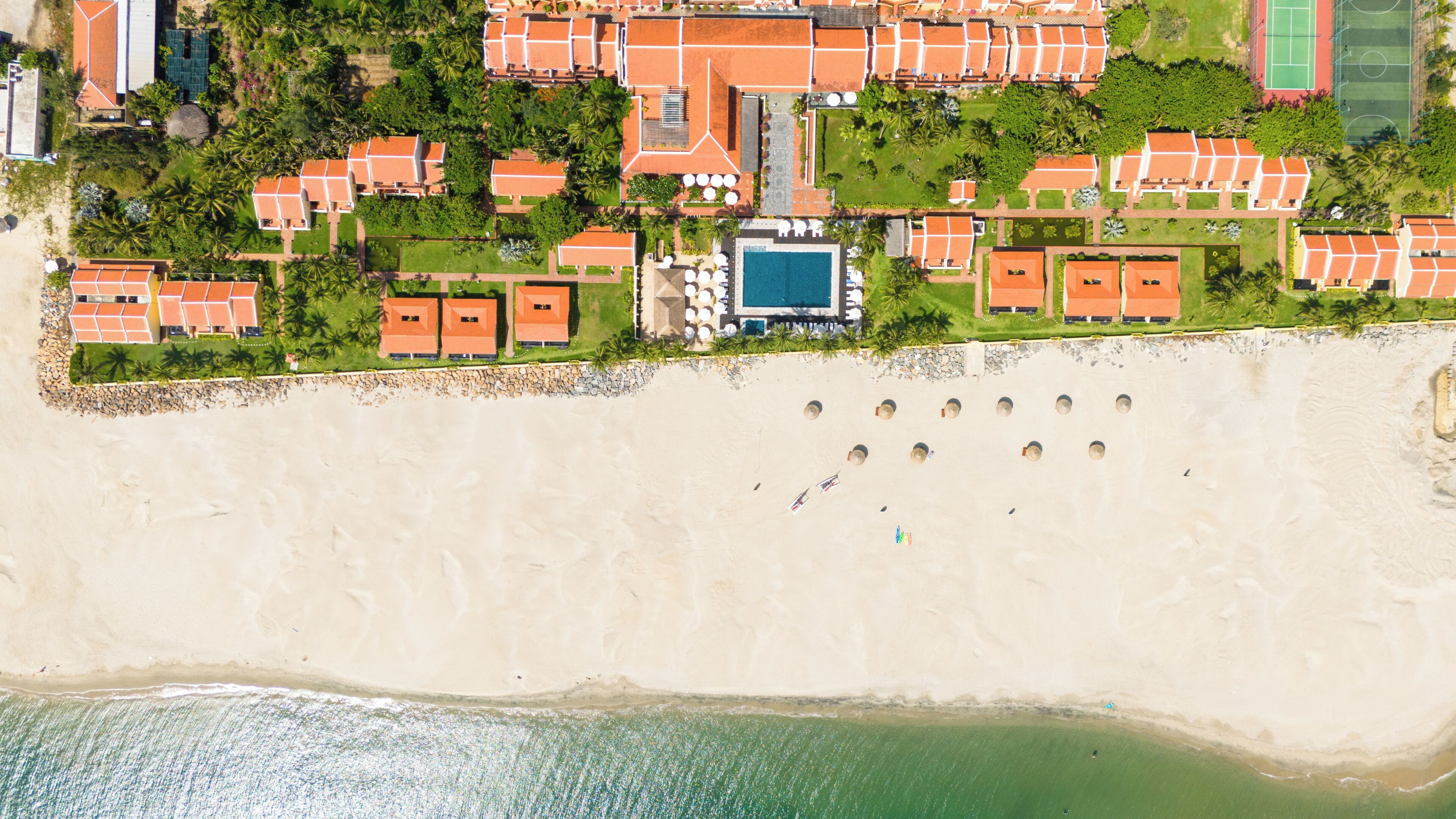 Vue aérienne d’un complexe hôtelier comprenant plusieurs bâtiments, une piscine et une plage.