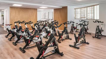 Un gimnasio con varias bicicletas estáticas dispuestas en filas, paredes con paneles de madera y ventanas amplias.