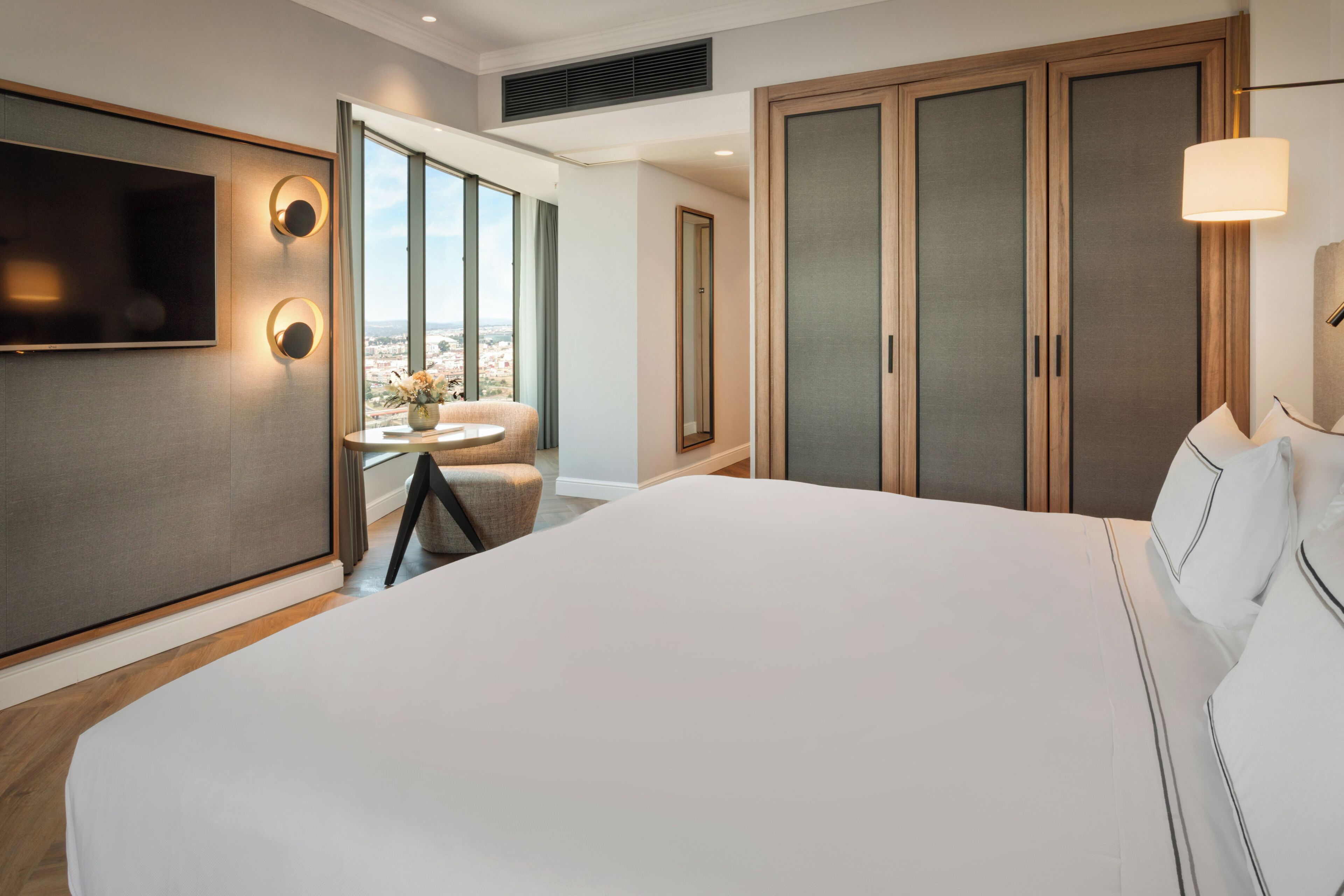 Een hotelkamer met een groot bed, een aan de muur bevestigde televisie, uitzicht op de stad door het raam en een inloopkast.