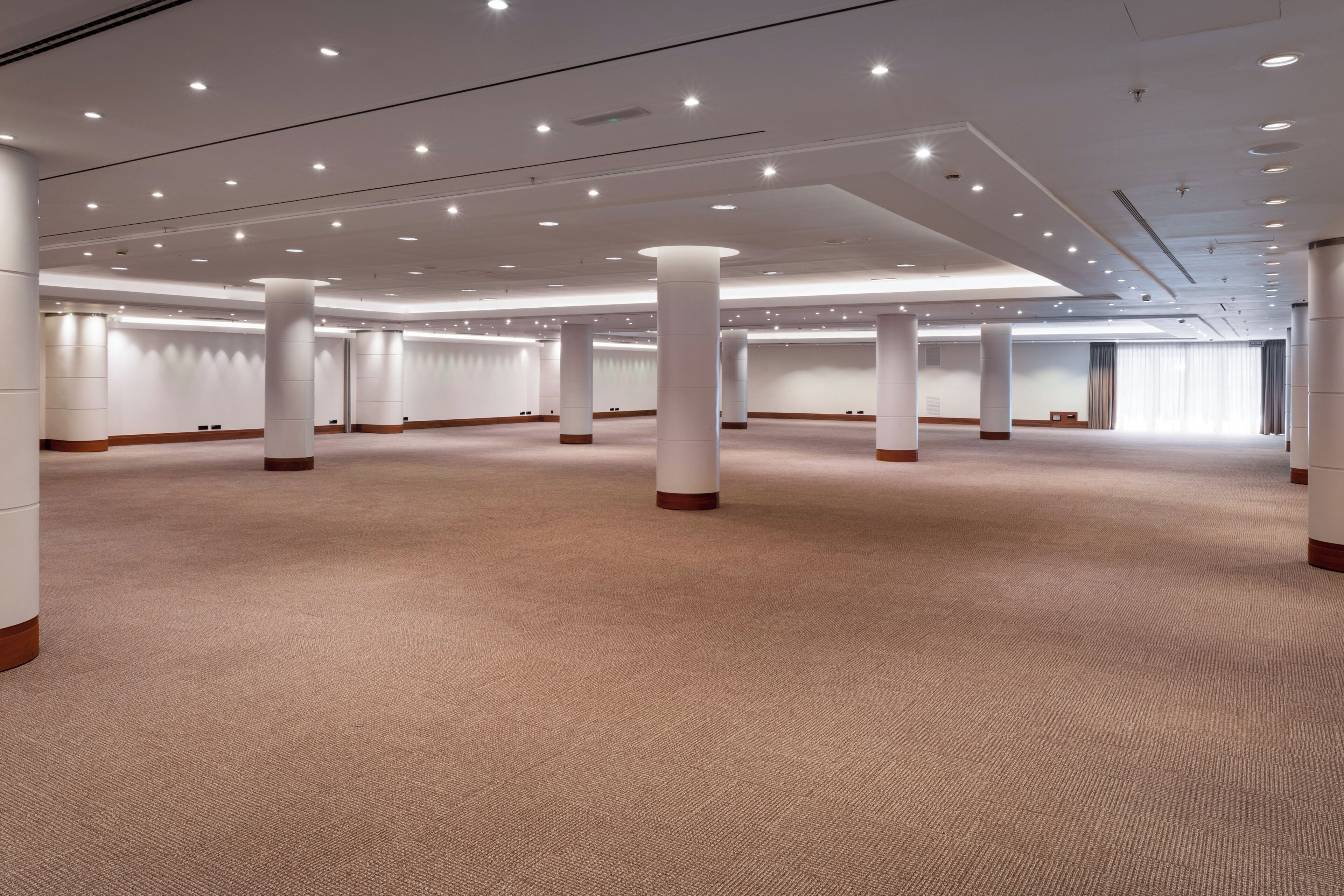 Una amplia sala de conferencias, bien iluminada, con techo alto, múltiples columnas y piso alfombrado.