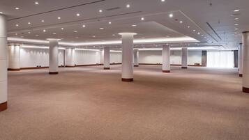 Una amplia sala de conferencias, bien iluminada, con techo alto, múltiples columnas y piso alfombrado.