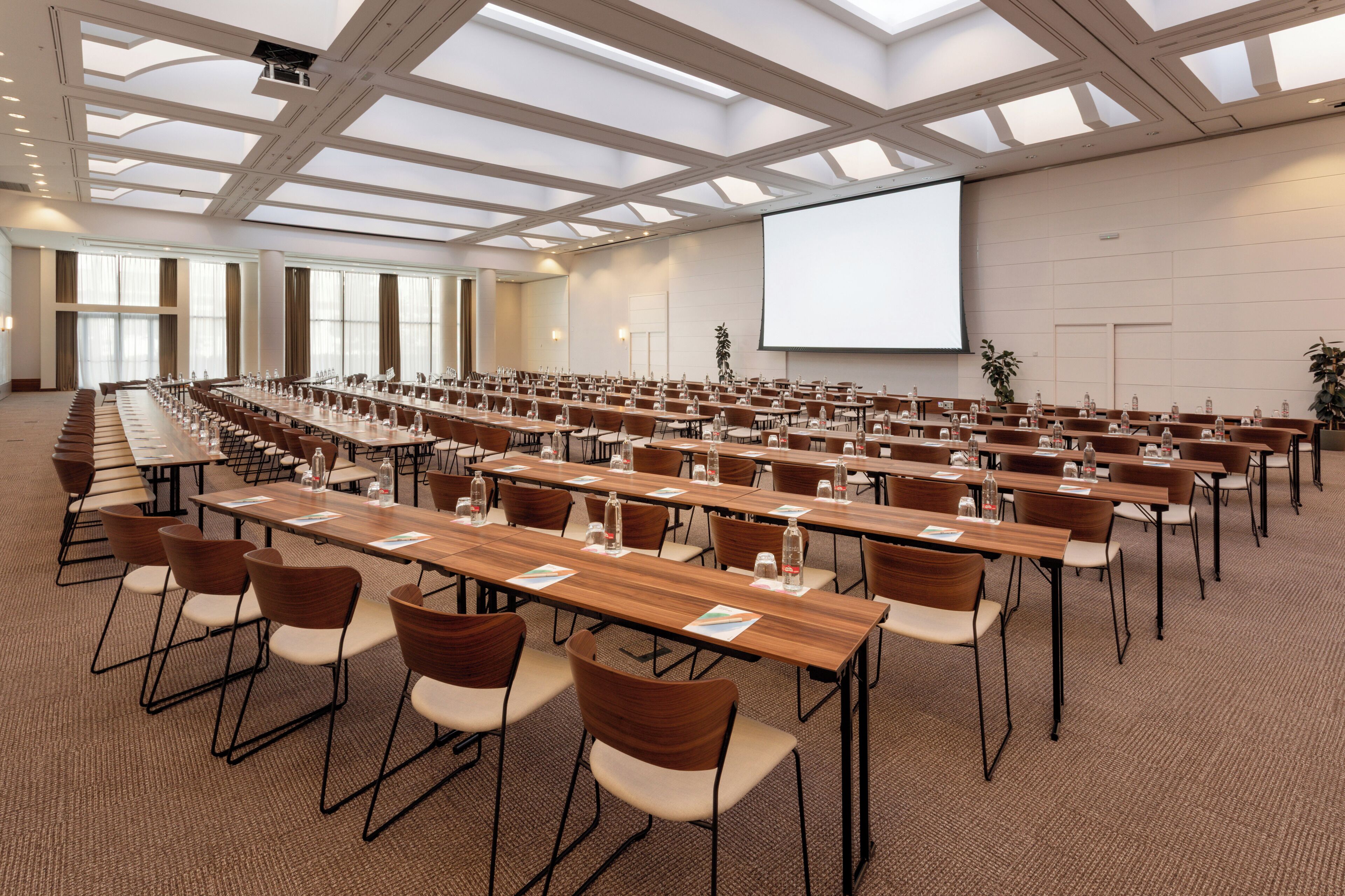 Un salón de conferencias con largas mesas, sillas y una pantalla grande.