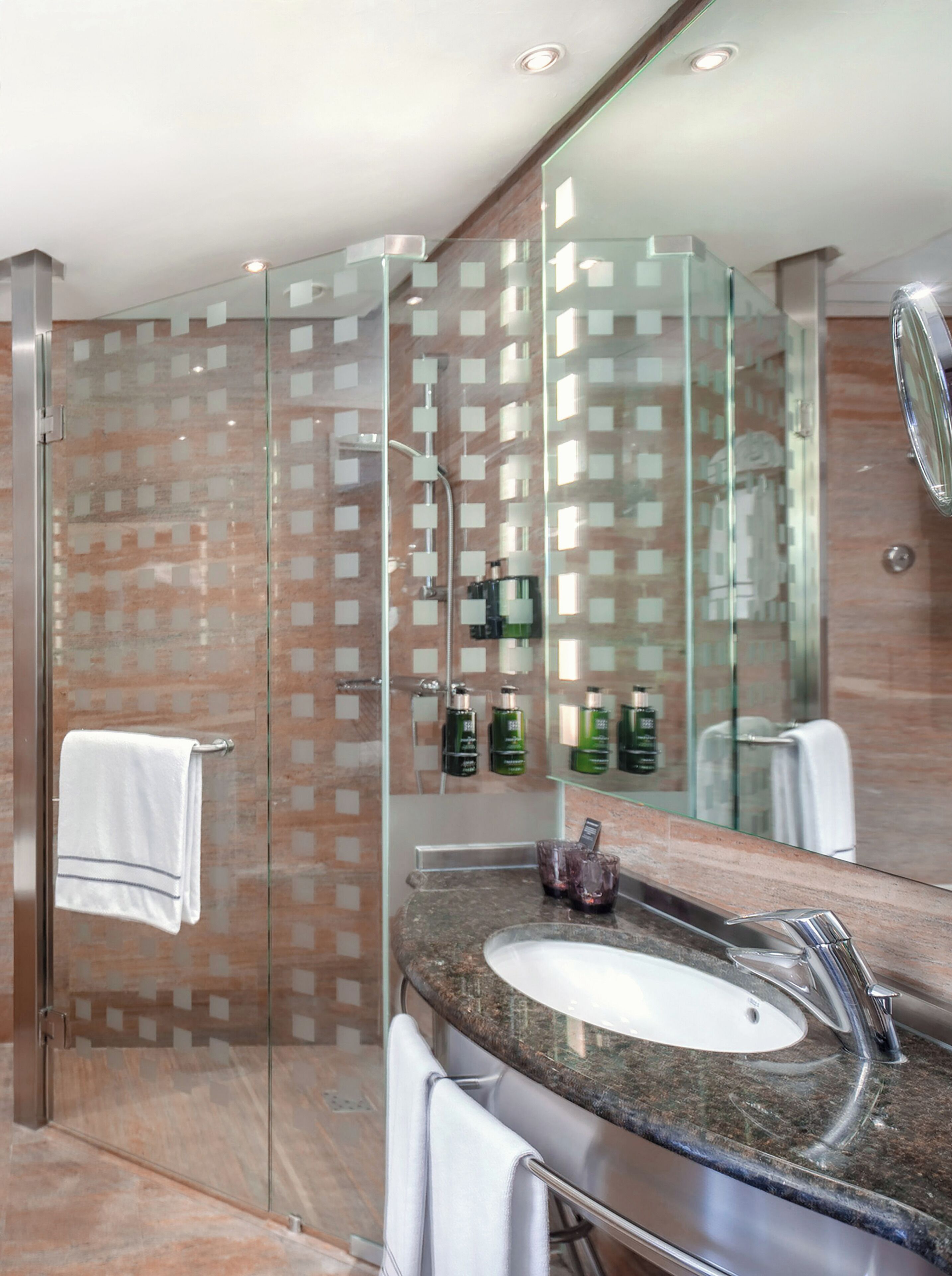 Un baño moderno con cabina de ducha de vidrio, lavabo con encimera de granito y un espejo grande.