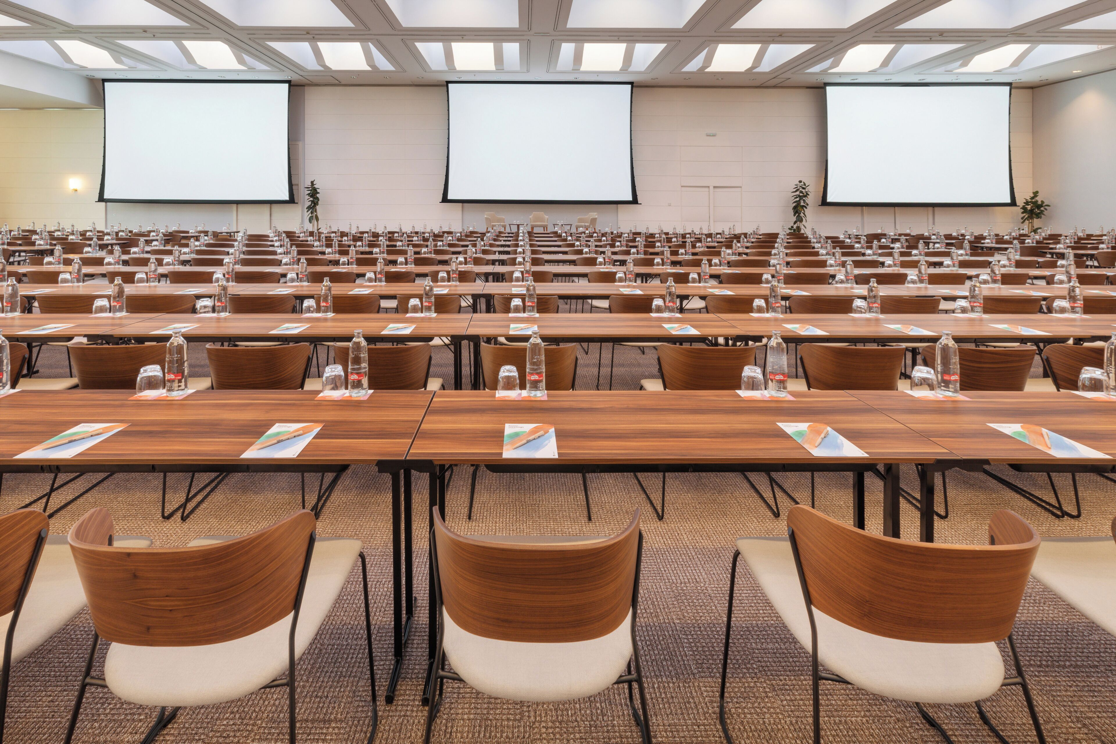 Un salón de conferencias con varias filas de mesas y sillas, equipado con botellas de agua y tarjetas de identificación.