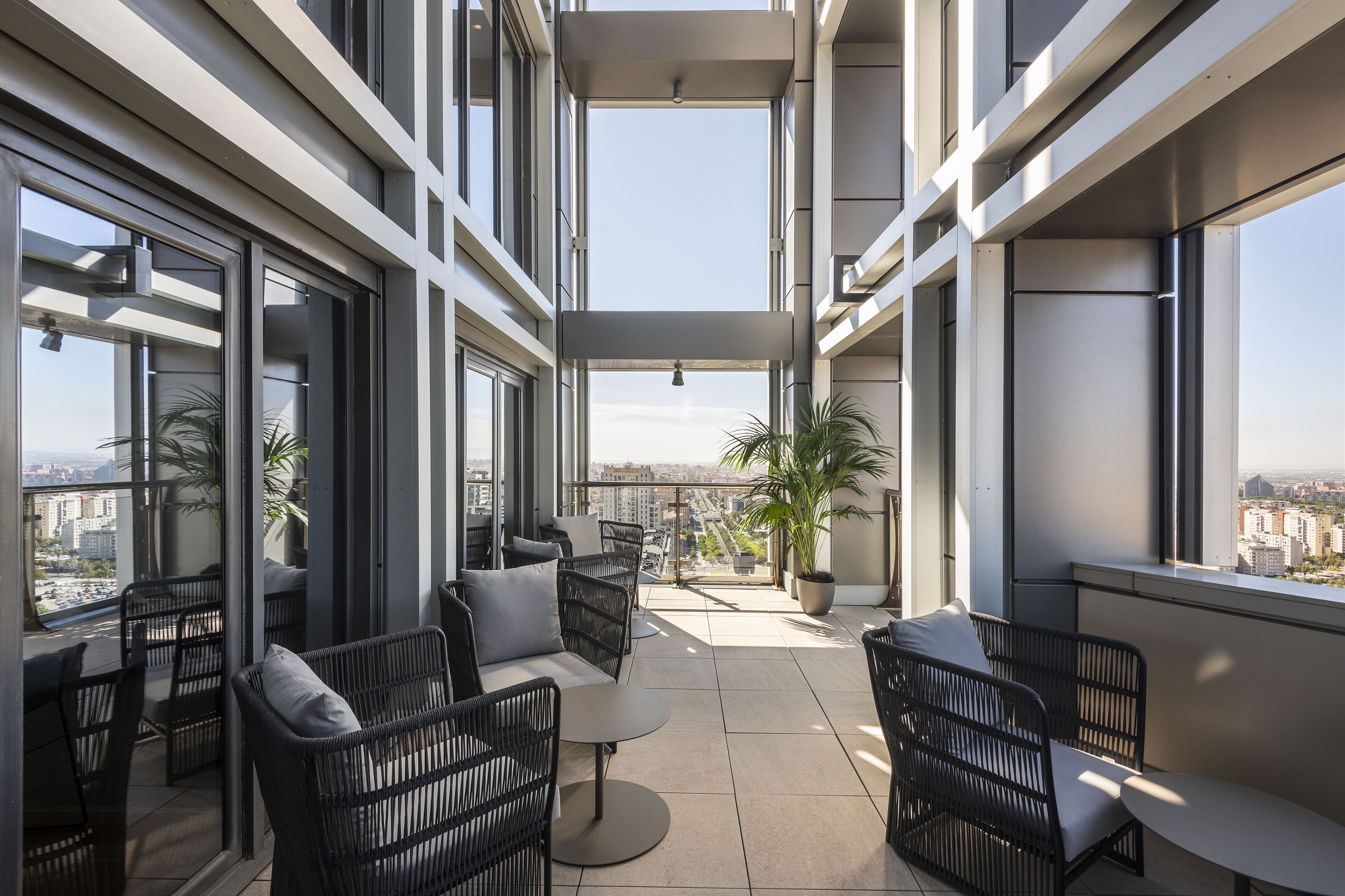 Un balcón moderno con mobiliario de mimbre, ventanas amplias y vistas a la ciudad.