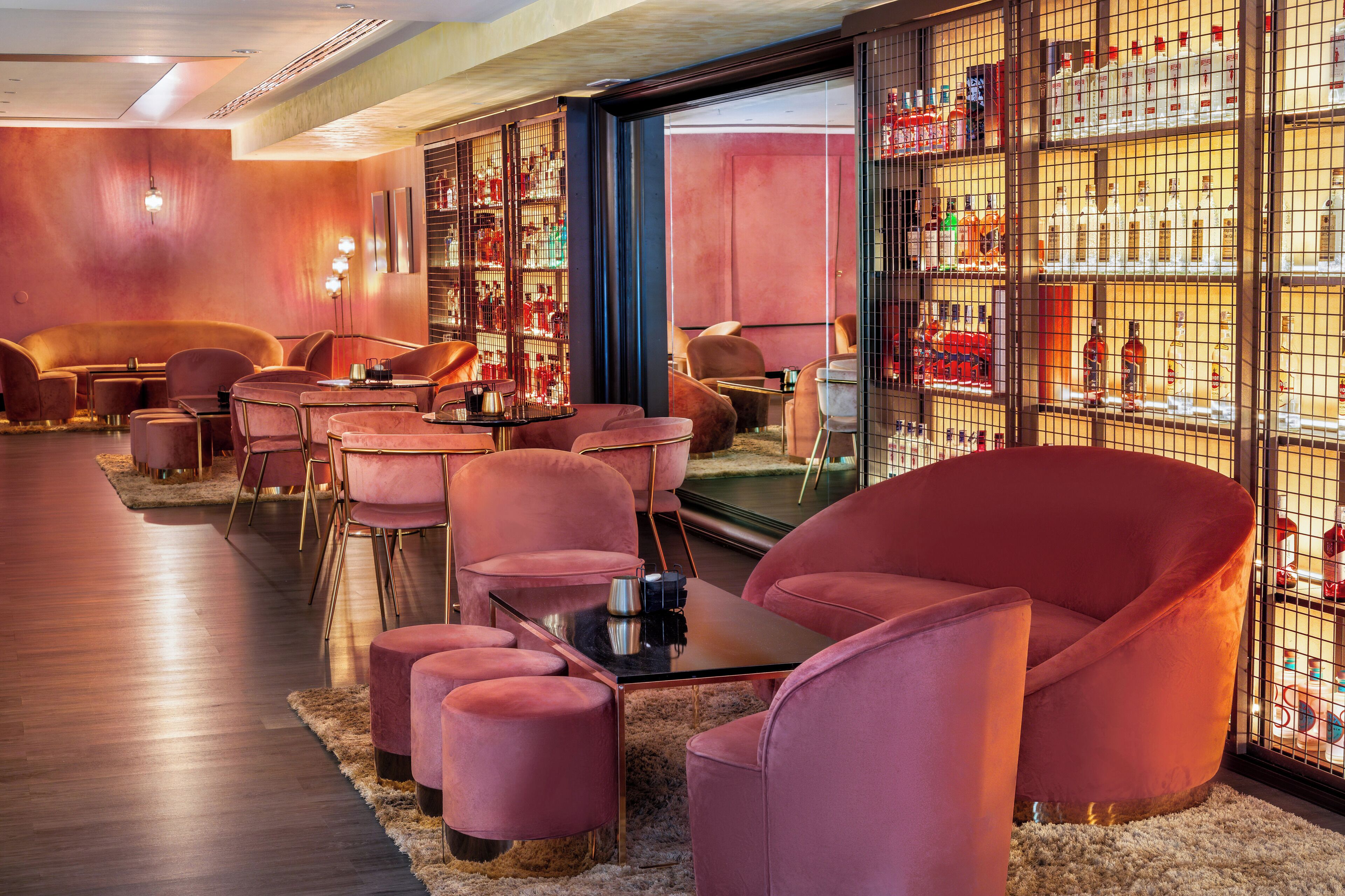 A modern bar area with plush seating, a glass display case with bottles, and a wooden floor.