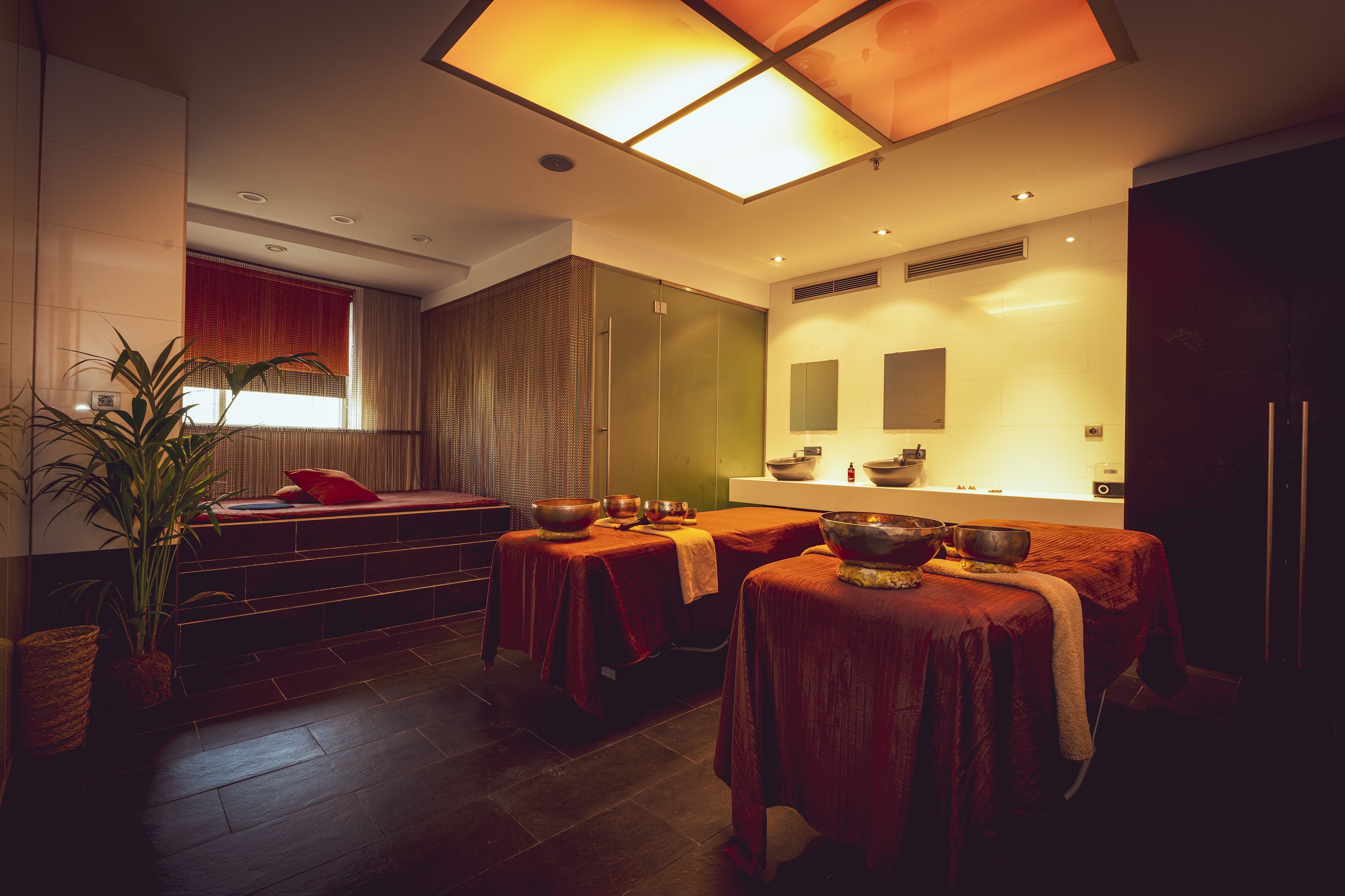 Un moderno cuarto de spa con una camilla de masaje, un amplio ventanal con cortinas y un mostrador de recepción.