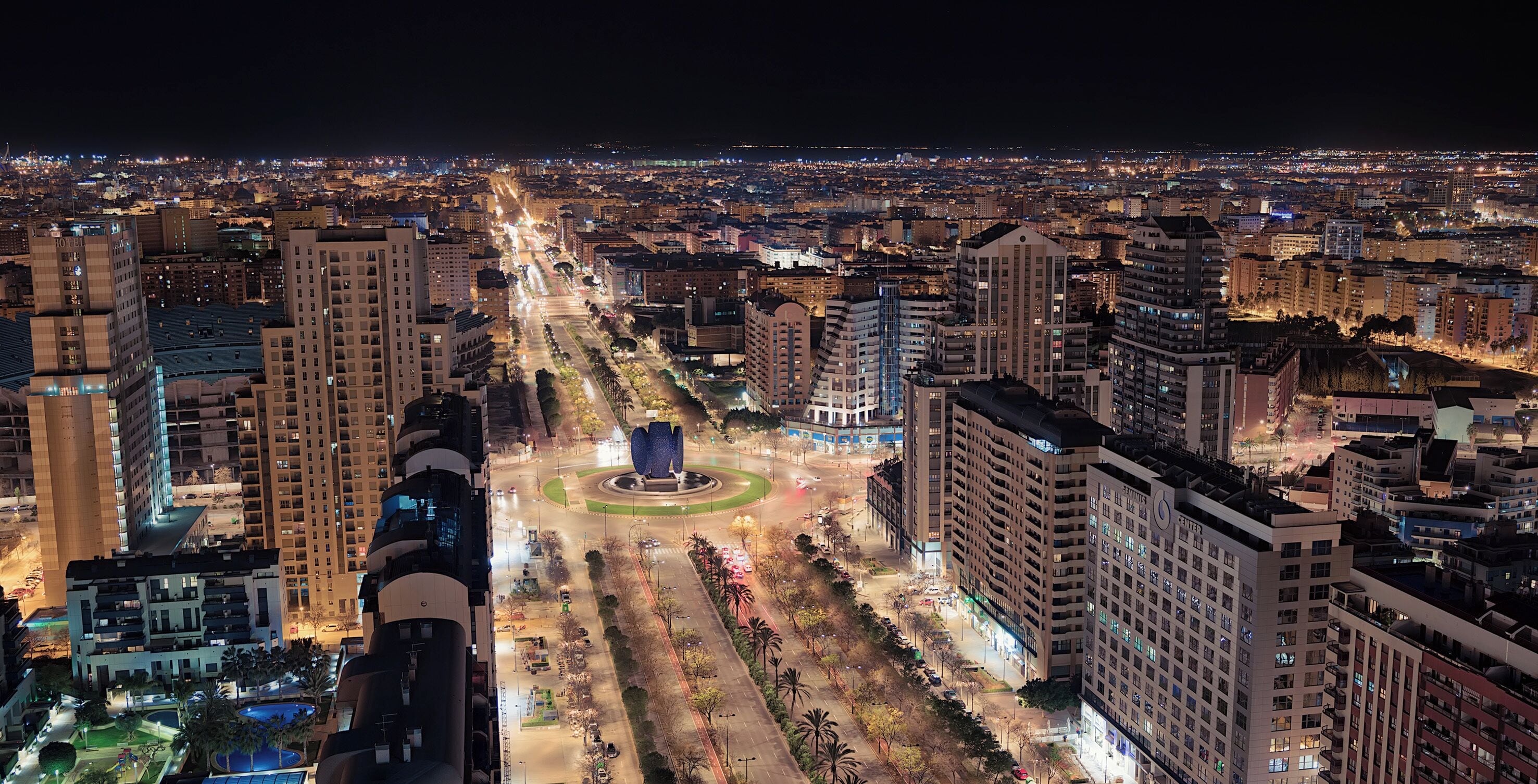 Un paisaje urbano nocturno con rascacielos, una rotonda central y un ambiente citadino bien iluminado.