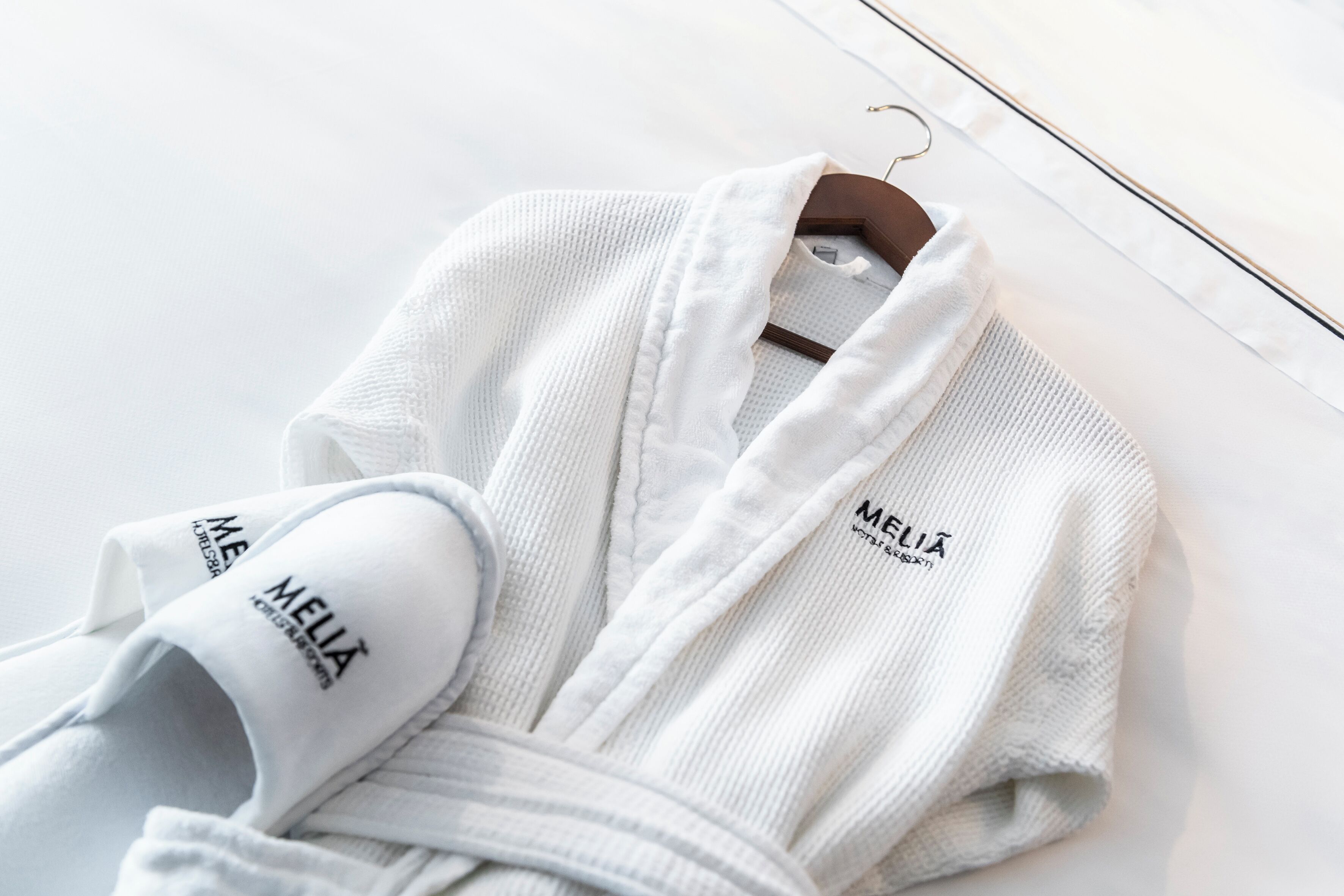 Ein weißer Bademantel mit 'MELIA'-Branding an einem Kleiderbügel.