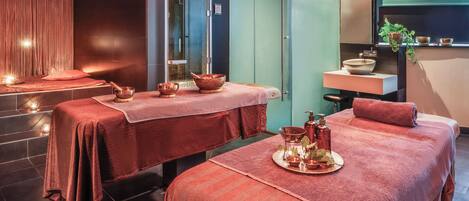 Sala de spa com duas macas de massagem, uma pia e um espelho.