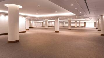Amplia habitación de hotel bien iluminada, con piso alfombrado, grandes pilares y un diseño moderno en el techo.