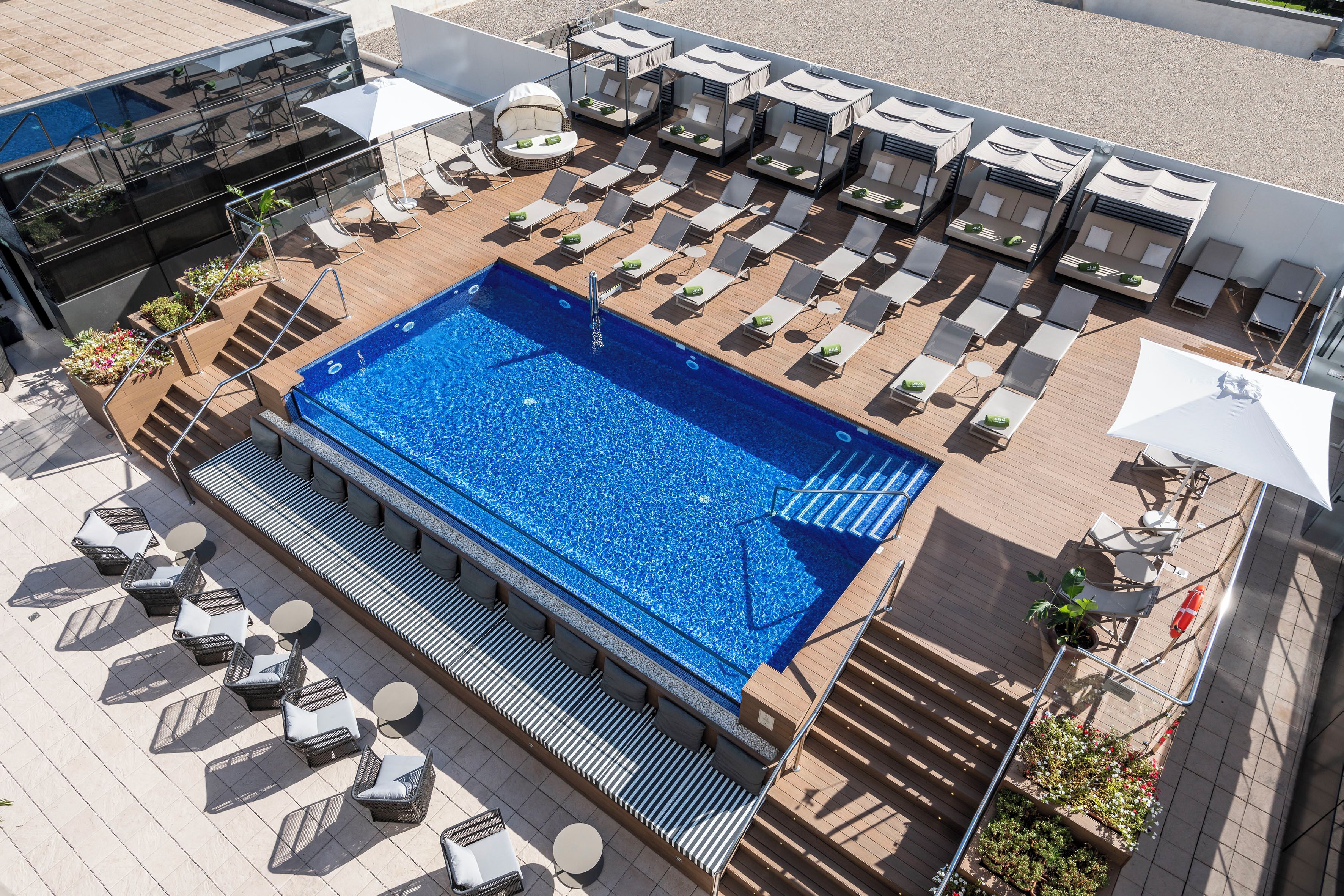 Un espace piscine sur le toit, comprenant des chaises longues, une piscine et un salon fermé par des baies vitrées.
