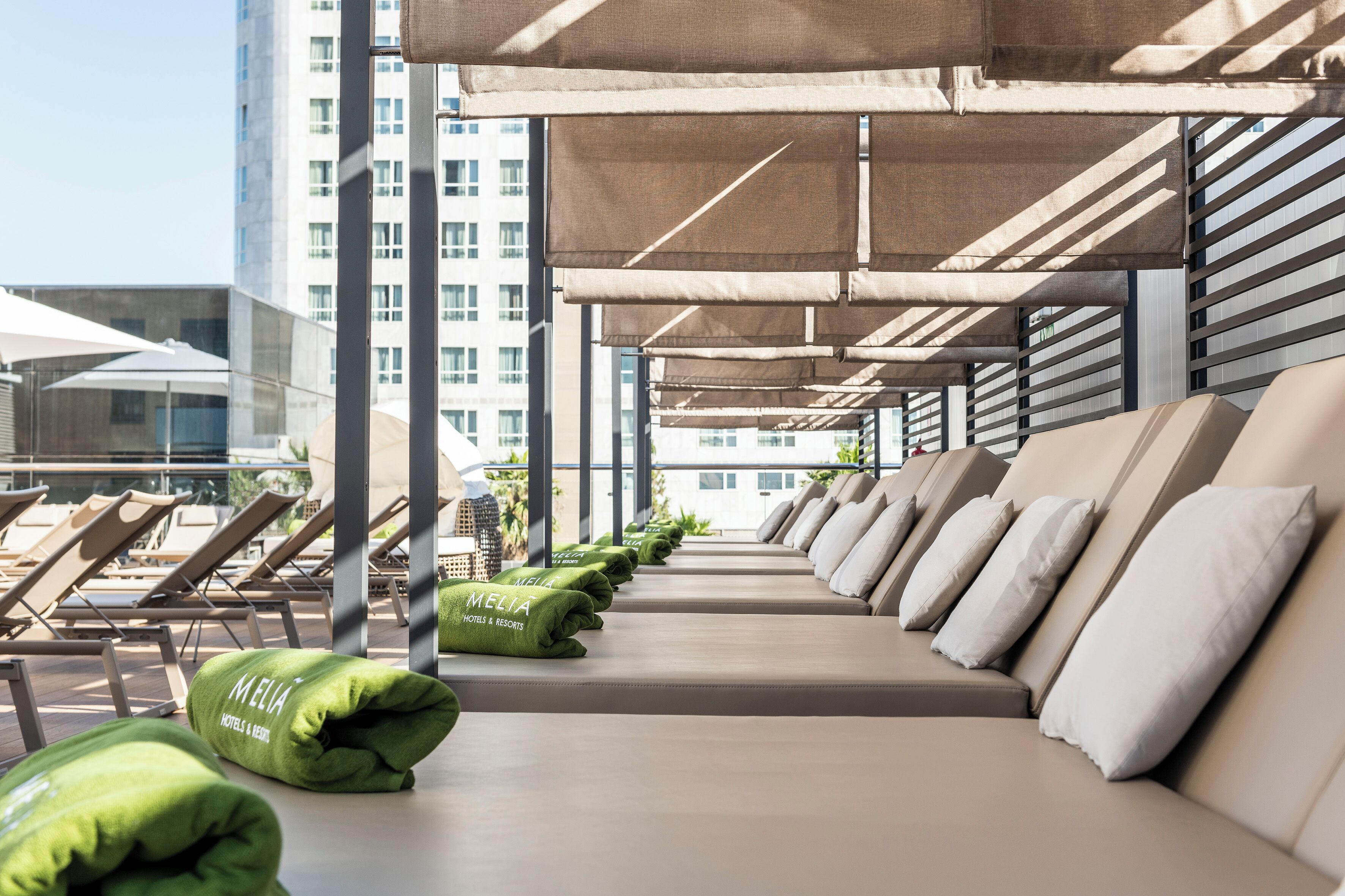 A row of lounge chairs and sofas under a canopy, with a building in the background.