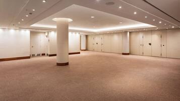 Un'ampia sala conferenze ben illuminata, con pavimento rivestito di moquette, diverse porte e luci a incasso nel soffitto.