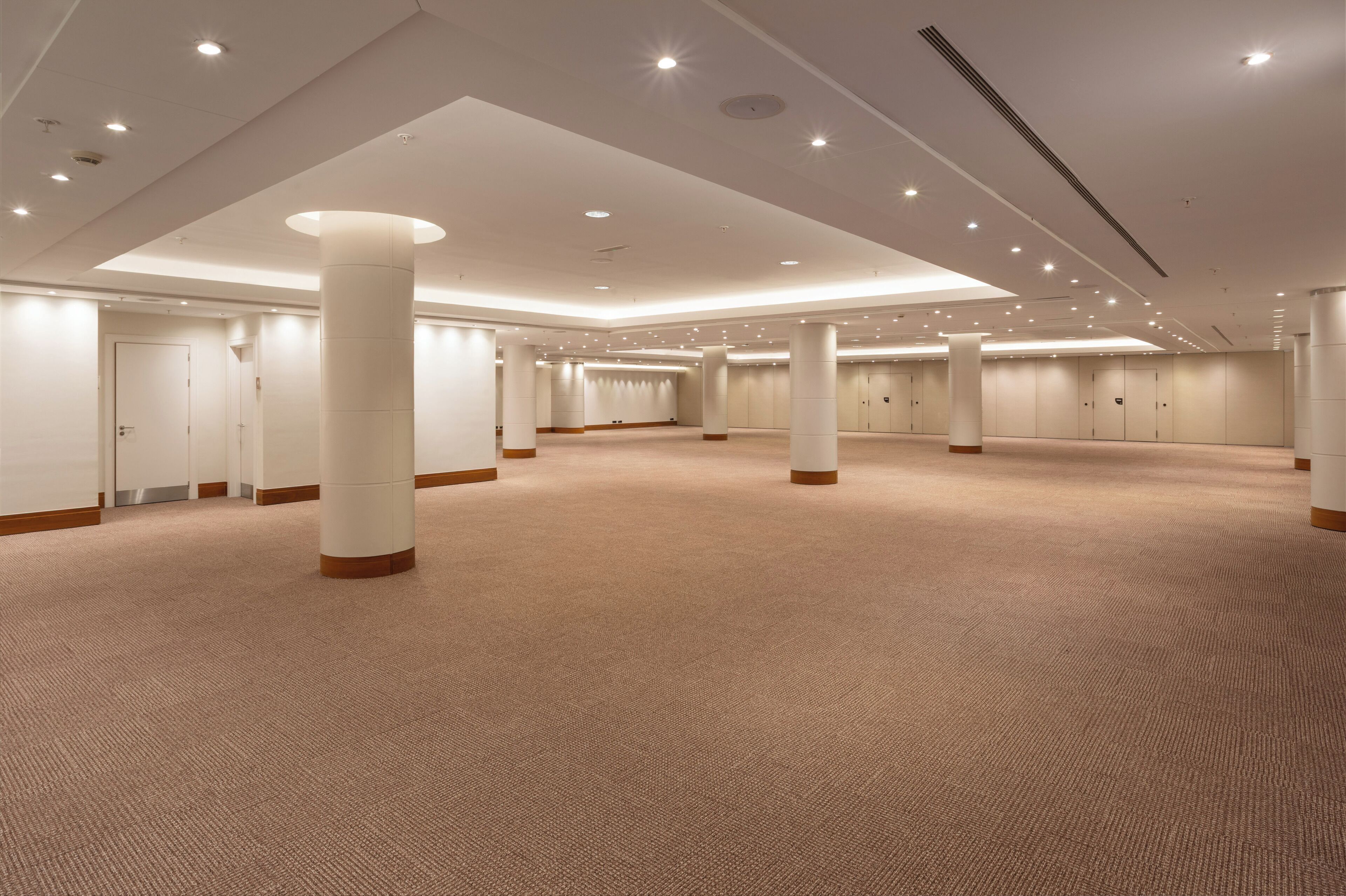 Un amplio hall de hotel con varias puertas, grandes pilares y piso alfombrado.