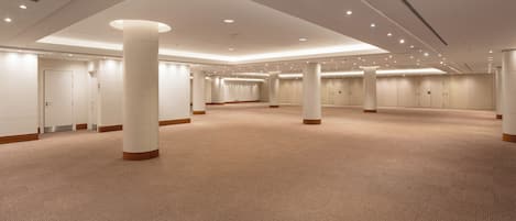 Un amplio hall de hotel con varias puertas, grandes pilares y piso alfombrado.