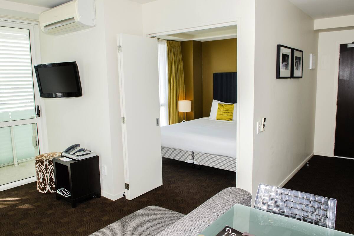 A hotel room with a bed, a television, a desk with a telephone, and a glass table.