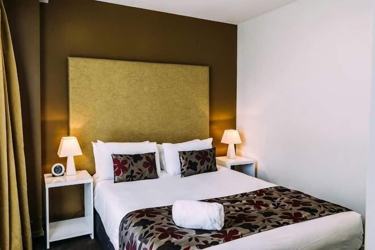 A hotel room with a large bed, two bedside tables, and a headboard.