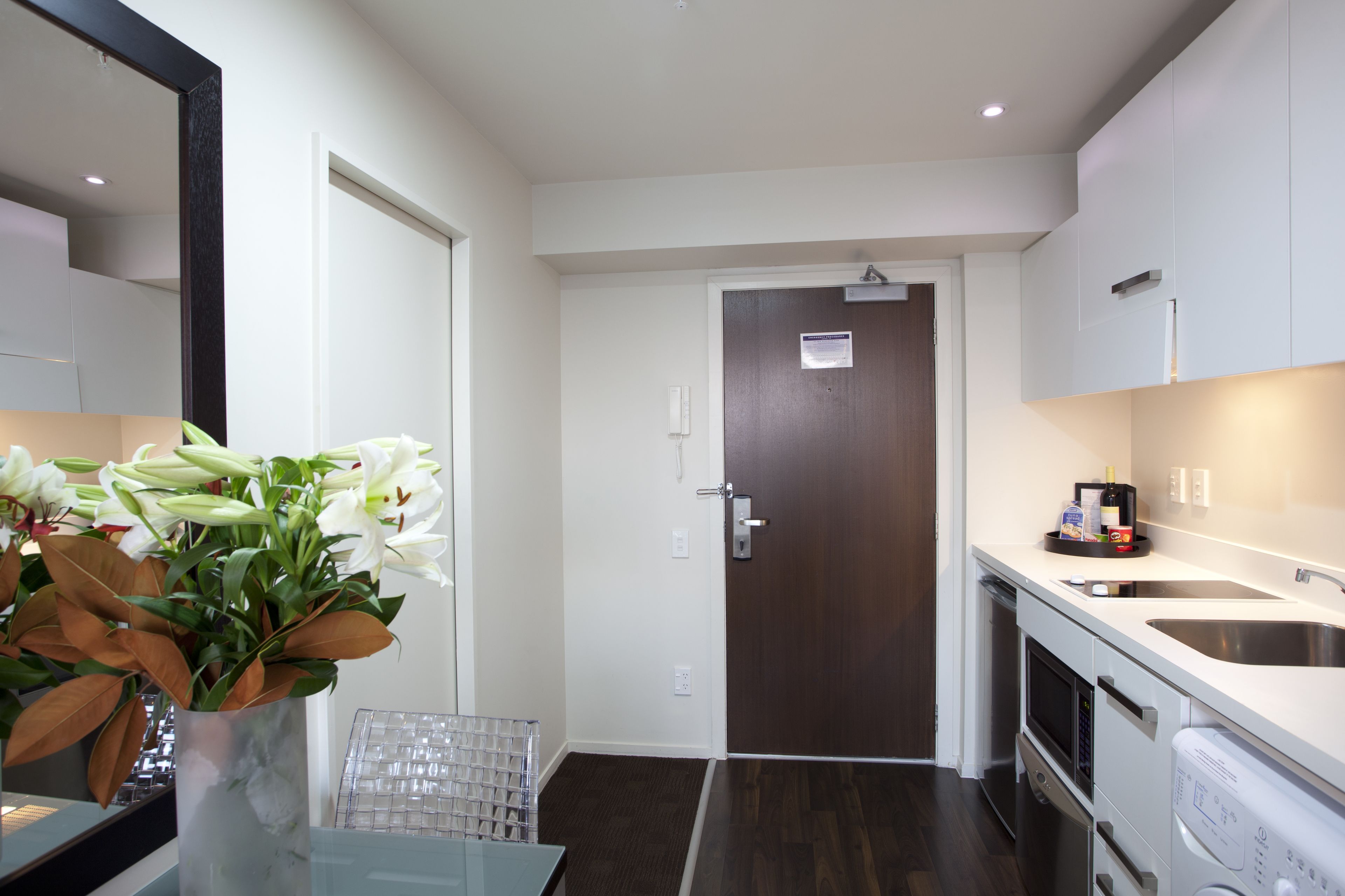 Una cocina moderna con armarios blancos, un lavamanos de acero inoxidable y un horno empotrado. Hay un jarrón con flores blancas sobre la encimera.