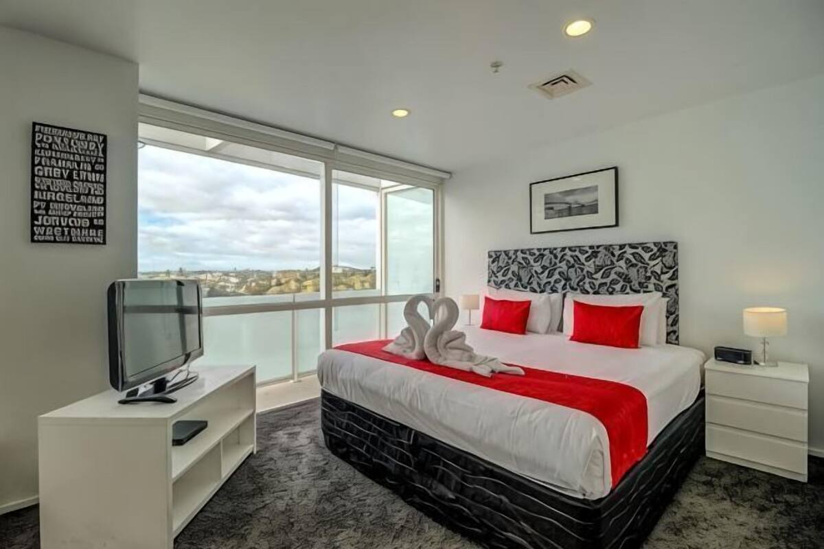 A hotel room with a large bed, a television, a view of the city, and a window.