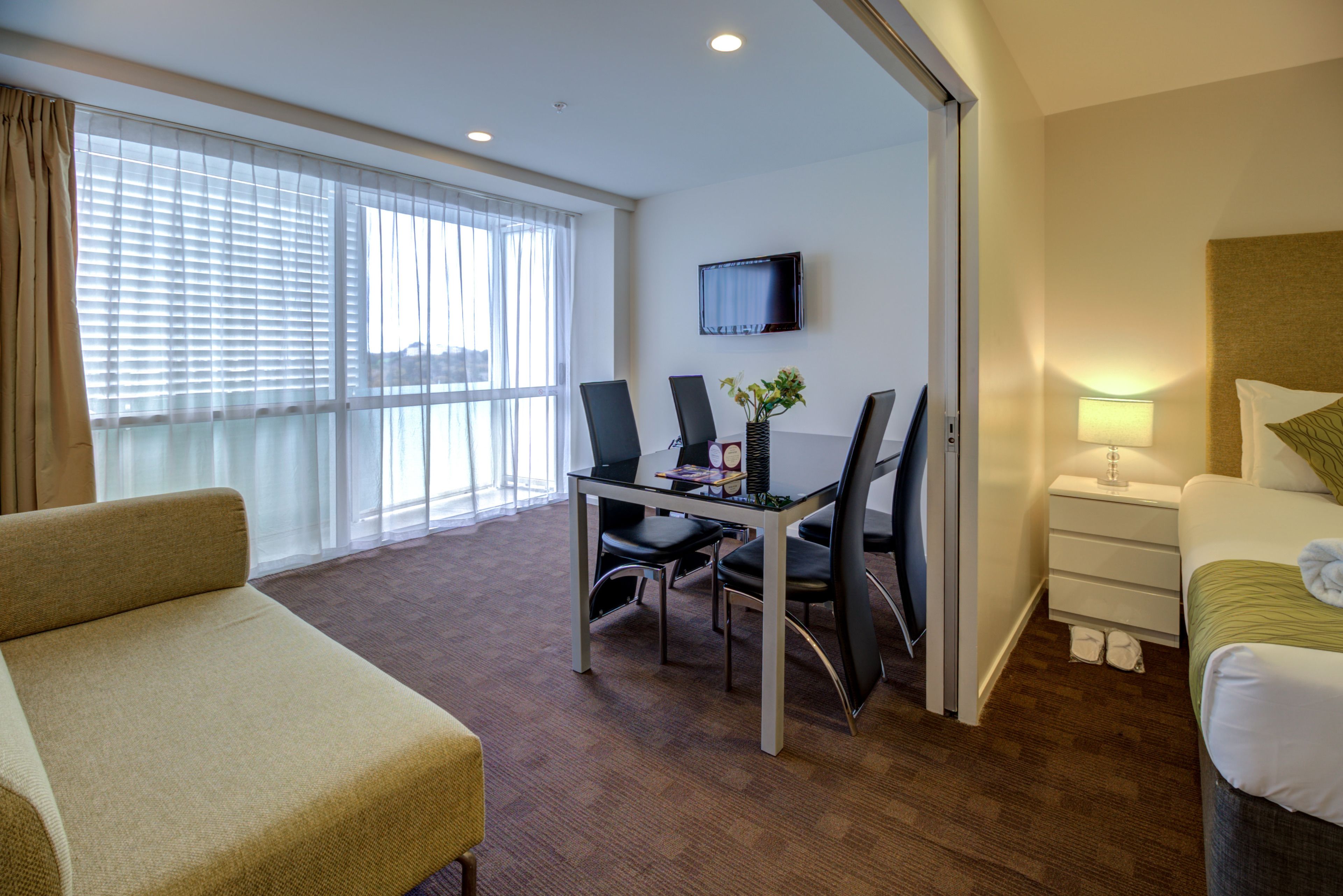 Une chambre d’hôtel comprenant un lit, un bureau avec deux chaises, une télévision et une fenêtre avec des rideaux.