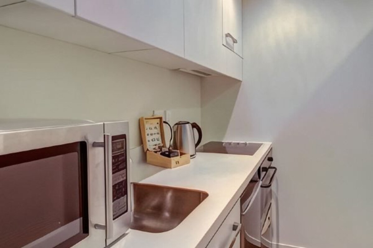 A kitchen with a microwave, kettle, and a wooden box with a kettle inside.
