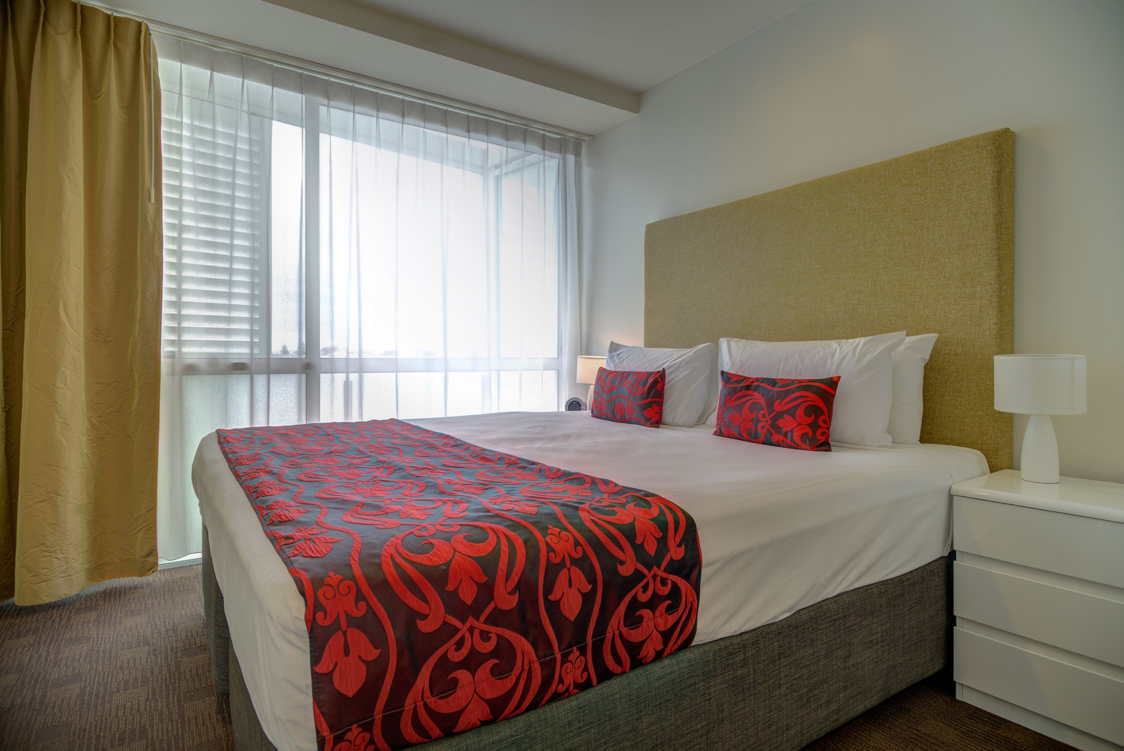 Una habitación de hotel con una cama grande, una mesita de noche con lámpara y una ventana con cortinas.