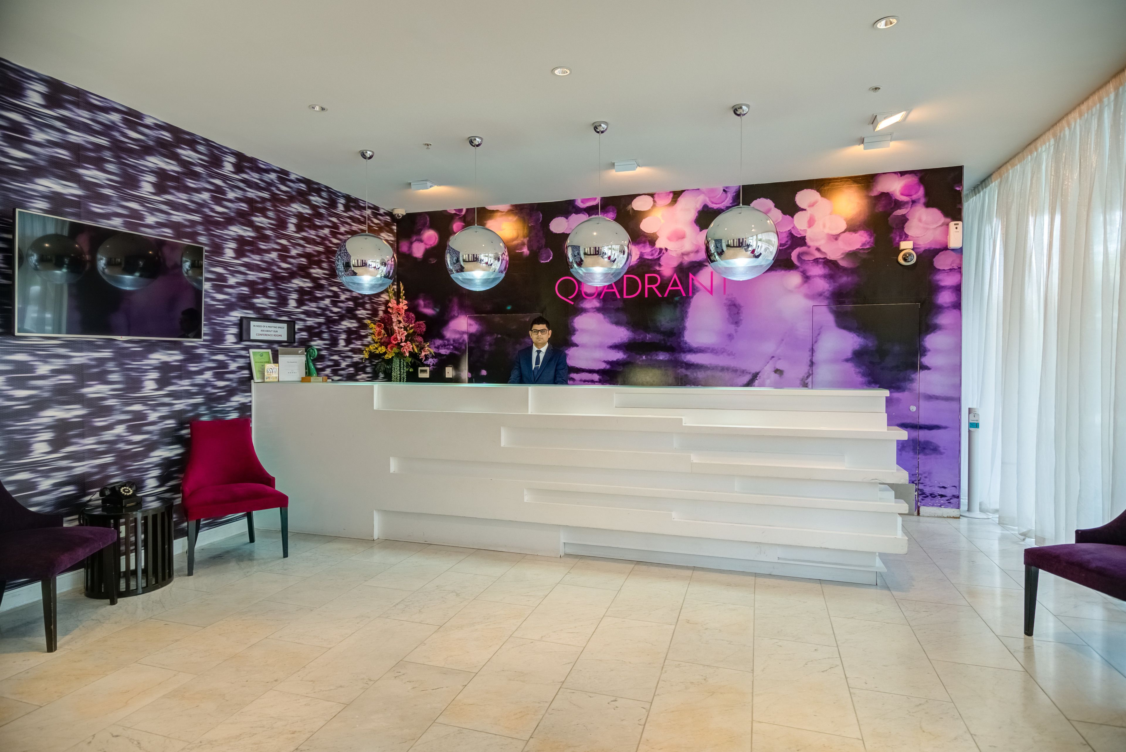 Ein Empfangsbereich im modernen Design mit einem weißen Empfangsschalter, violetten und pinkfarbenen Wanddekorationen und einer Neonleuchtreklame.