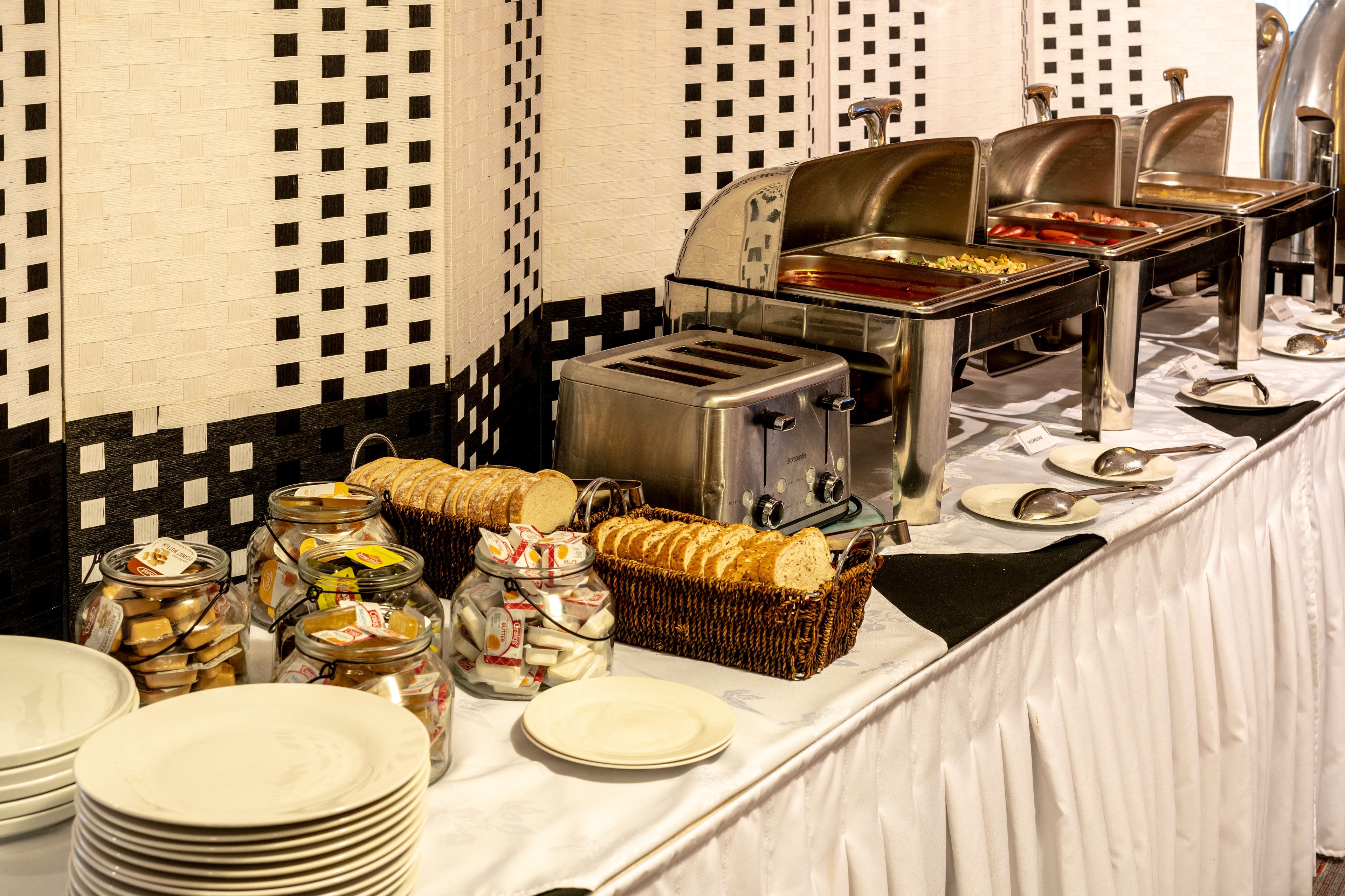 Un buffet proposant une variété de plats, notamment du pain, du fromage et des condiments, disposés sur une table devant un mur à carreaux.
