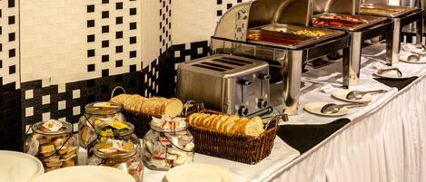 Un buffet proposant une variété de plats, notamment du pain, du fromage et des condiments, disposés sur une table devant un mur à carreaux.