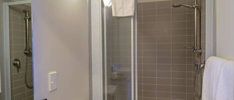 Une salle de bain équipée d’un lavabo, de toilettes et d’une douche séparée par des parois en verre.