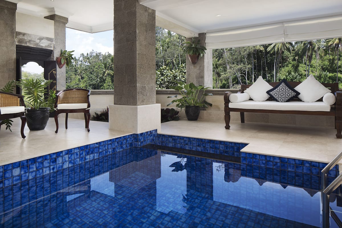 A pool area with a blue tiled floor, a white sofa with cushions, and potted plants.