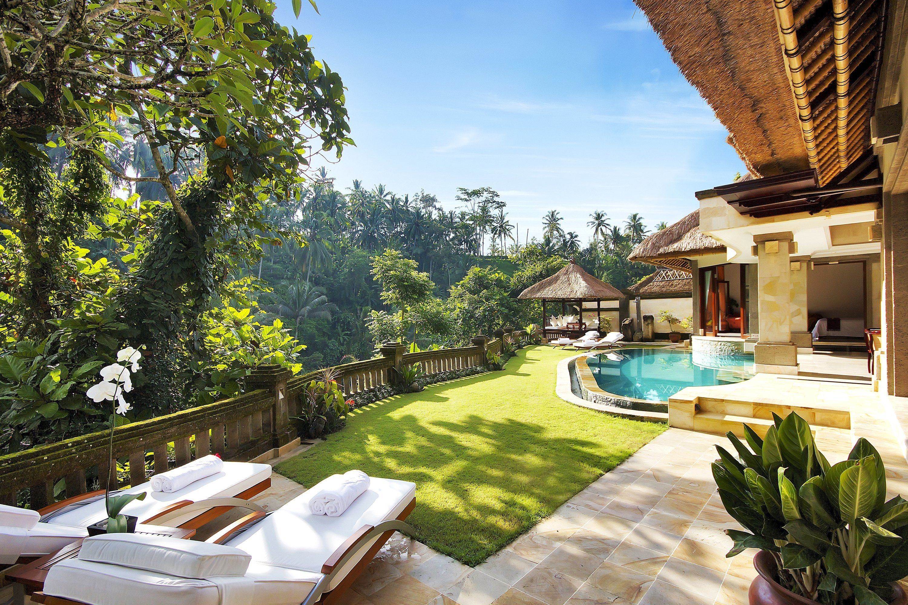 A poolside area with lounge chairs, a well-maintained lawn, and a clear view of the surrounding tropical landscape.
