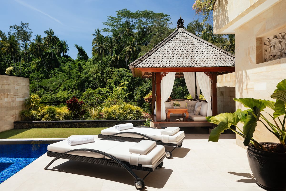 A poolside area with two lounge chairs, a gazebo, and a potted plant.