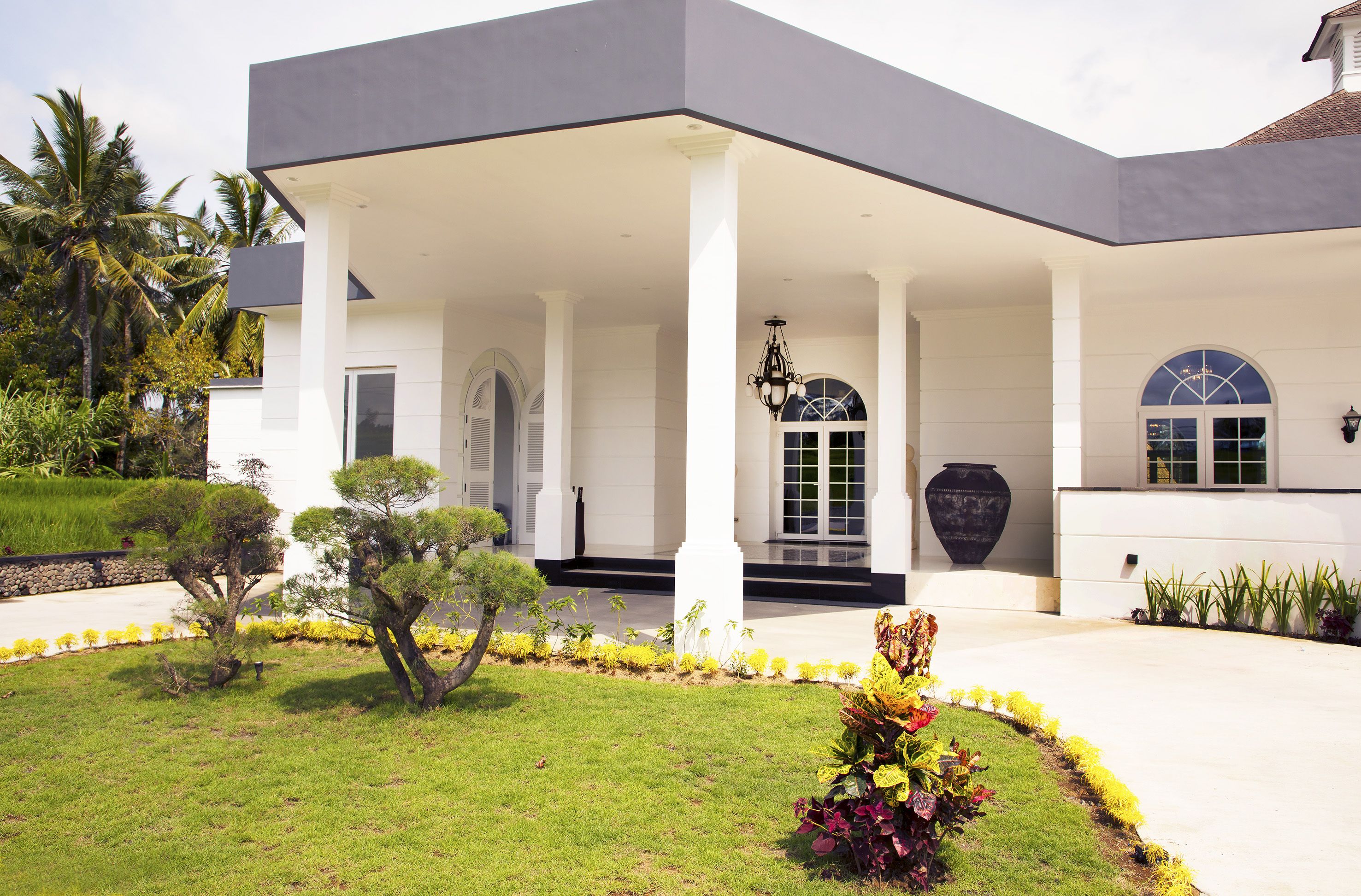 A modern building with a covered entrance, columns, and a well-maintained garden with various plants and a pathway leading to the entrance.