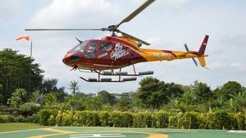 Un helicóptero rojo y amarillo con la marca "Sky Tours", sobrevolando un campo verde con un gran logotipo amarillo y verde.