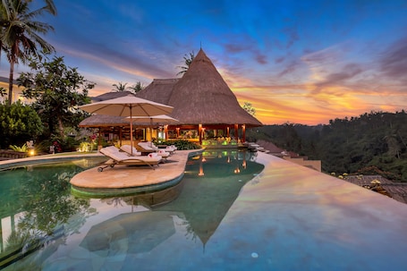 A resort with a pool, lounge chairs, and a thatched-roof building.