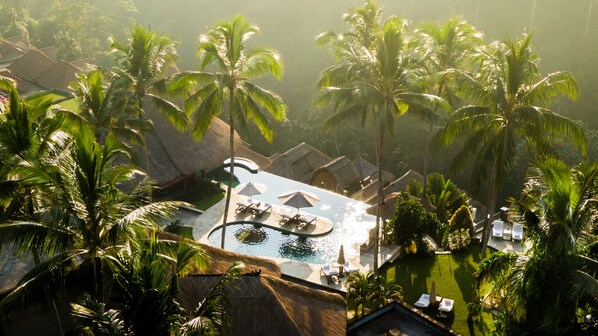 A resort with a pool surrounded by palm trees and thatched-roof structures. - Viceroy Bali (Ubud)