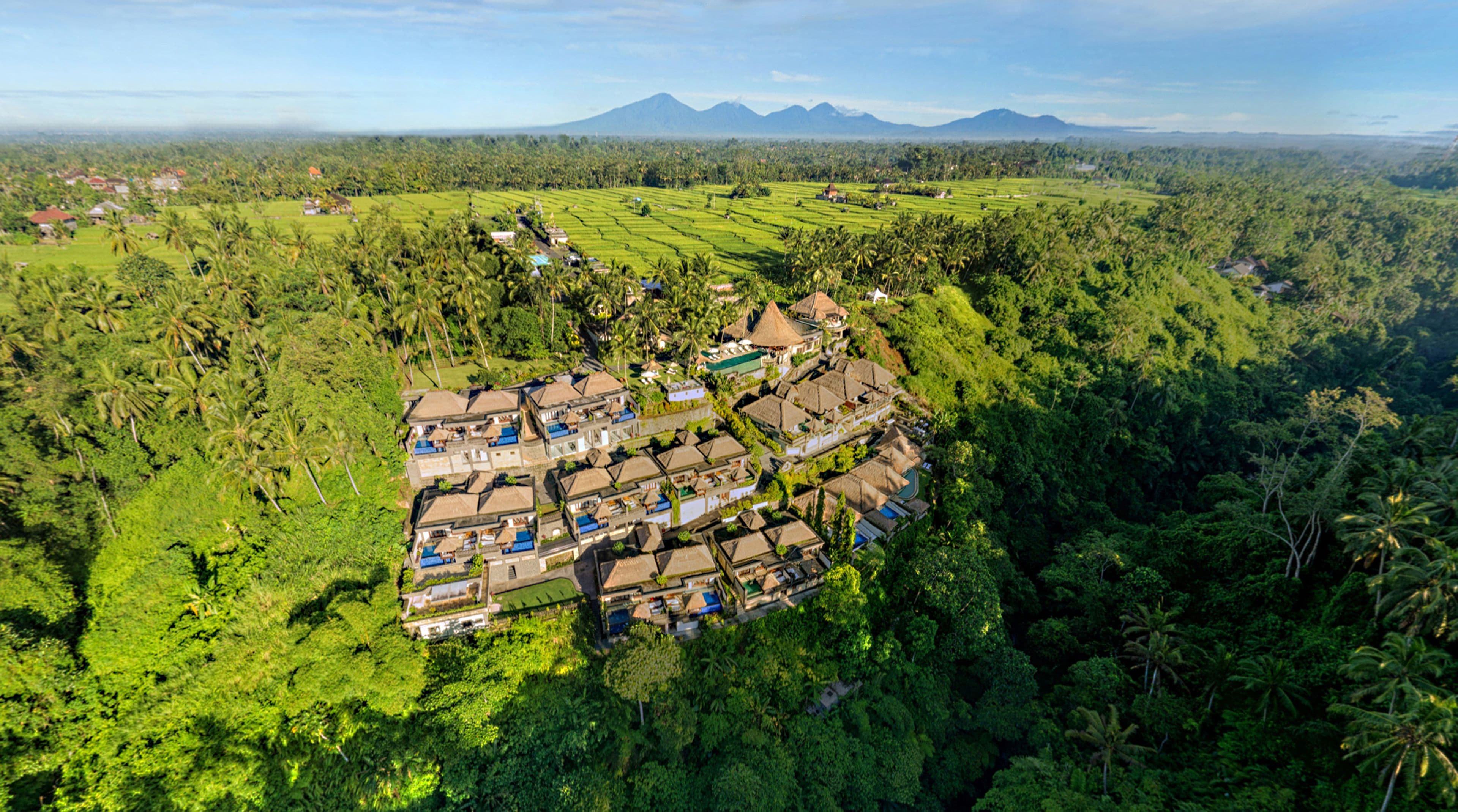 An aerial view of a resort with multiple bungalow-style buildings, surrounded by lush greenery and palm trees.
