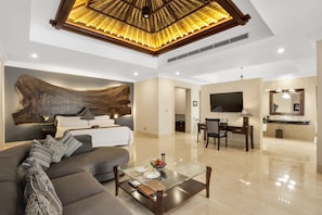 A modern living room with a sofa, coffee table, and a large wooden headboard. There is a dining area with a table and chairs, and a bathroom with a sink and mirror.