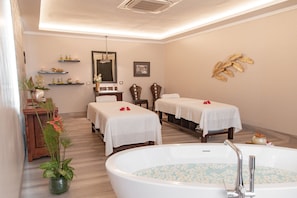 A spa room with two beds, a large bathtub, and a mirror above the bed.