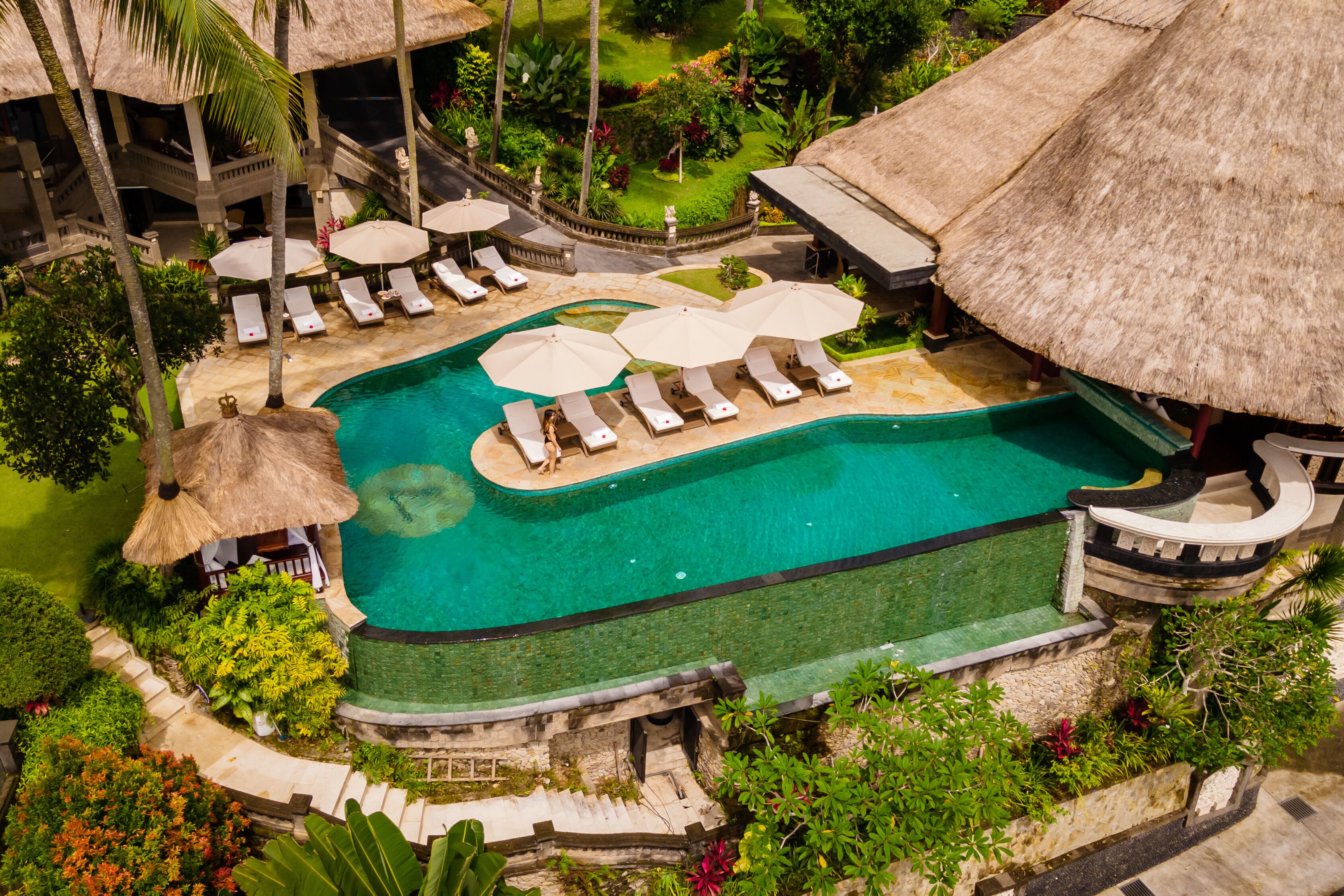 An aerial view of a resort with a swimming pool, lounge chairs, and thatched-roof structures.