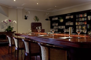 A bar area with a long wooden counter, wicker chairs, and a bookshelf filled with books and magazines.