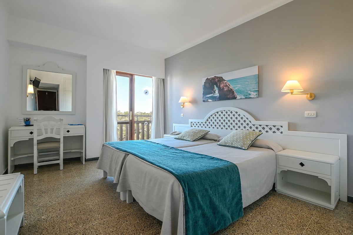 A bedroom with a bed, bedside tables, a desk, a chair, and a window with a view.